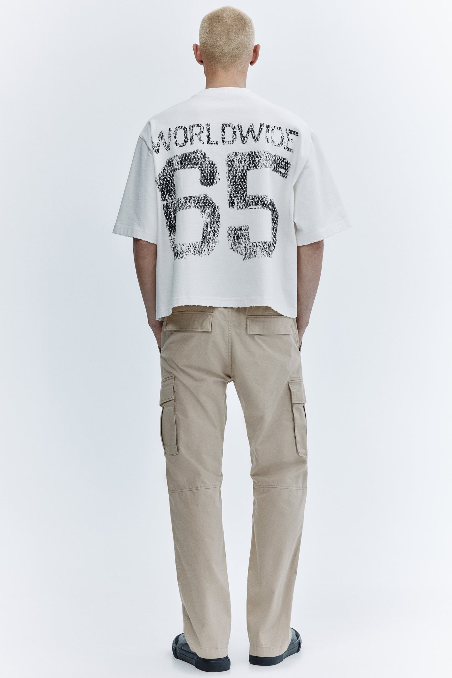 Person wearing a white t-shirt with text and beige cargo pants on a white background