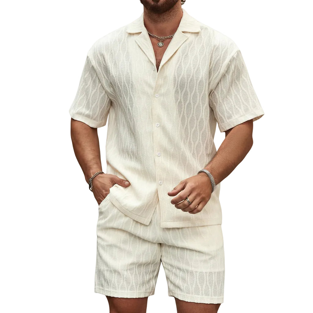 Man wearing a white textured shirt and shorts set against a stone wall.
